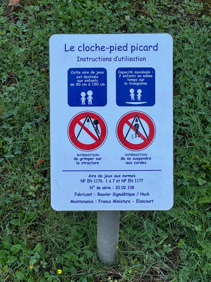 Panneau d'une aire de jeux mentionnant les normes NF EN 1176-1 à 7 et NF EN 1177, avec numéro de série, fabricant et prestataire de maintenance